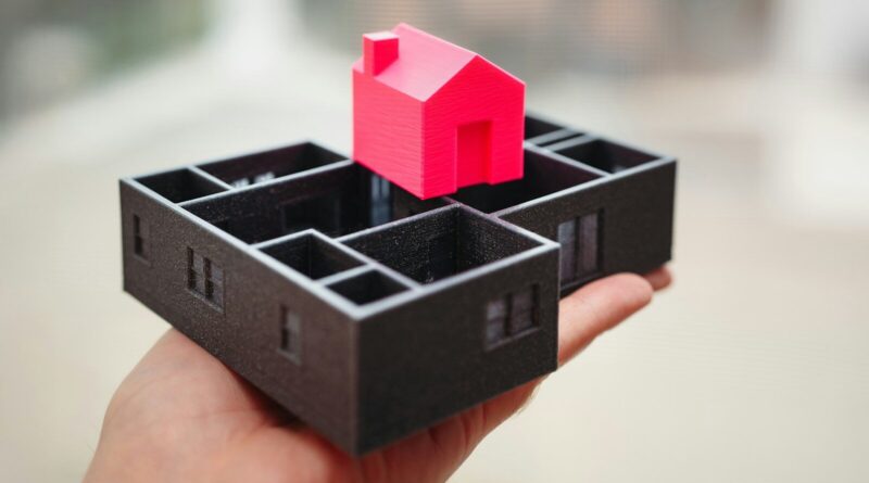 A hand holding a black box with a red house in it